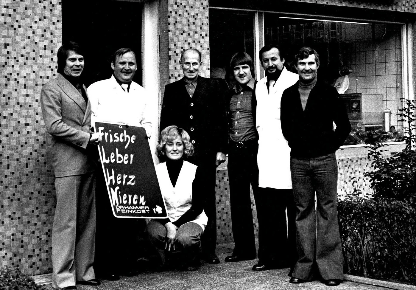 Gisela Zarges, vorne kniend, mit dem Team der Metzgerei Zarges vor dem Laden, historische Aufnahme